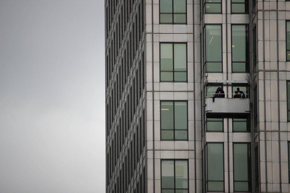 Window cleaners working on a platform on a modern high-rise building on a cloudy day.